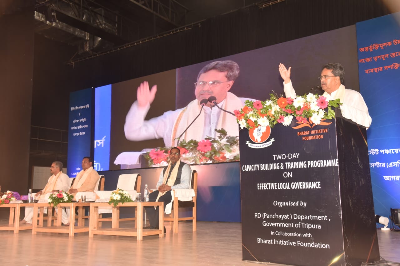 A speaker at the Bharat Initiative Foundation podium, with the address shown on the screen behind the stage