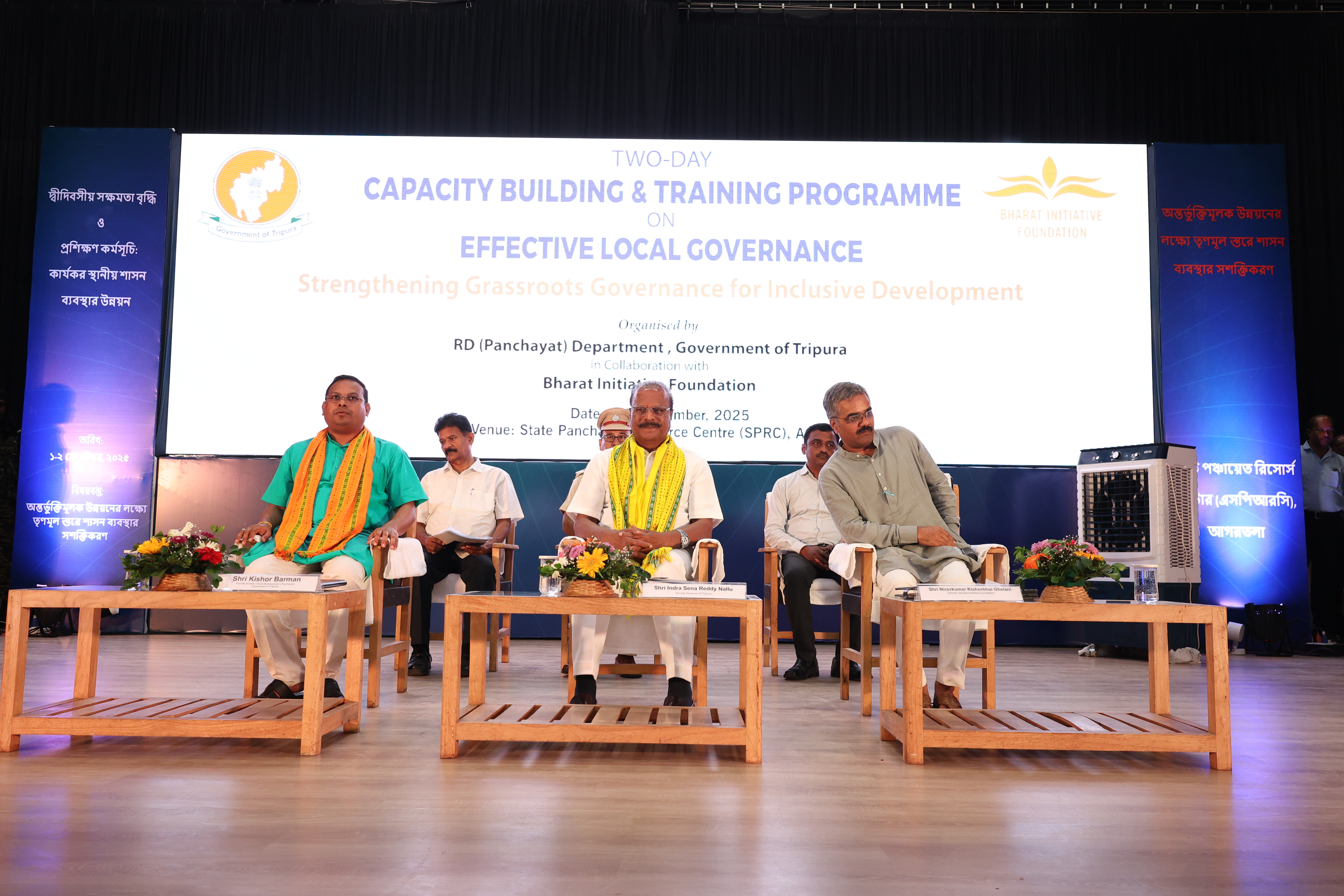 A panel seated on stage during a discussion, with floral arrangements on the tables