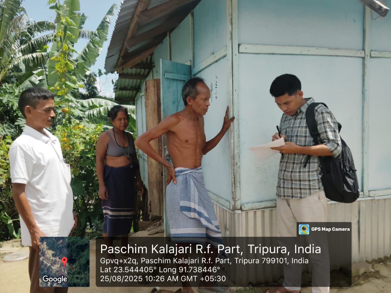 A field investigator taking notes outside a home in Paschim Kalajari while residents look on