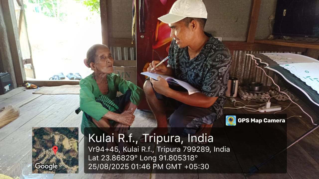 A field investigator seated with an elder, writing responses in Kulai