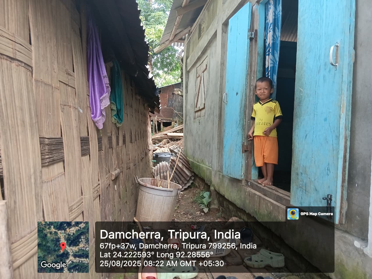 A child standing in a blue doorway along a narrow lane in Damcherra